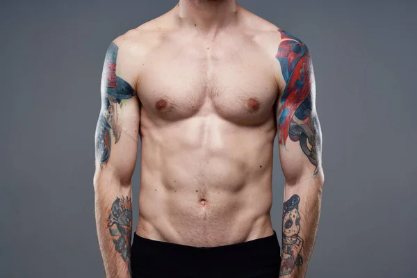 Deportivo hombre con bombeado hasta abdominales tatuajes en sus brazos gris fondo músculos — Foto de Stock