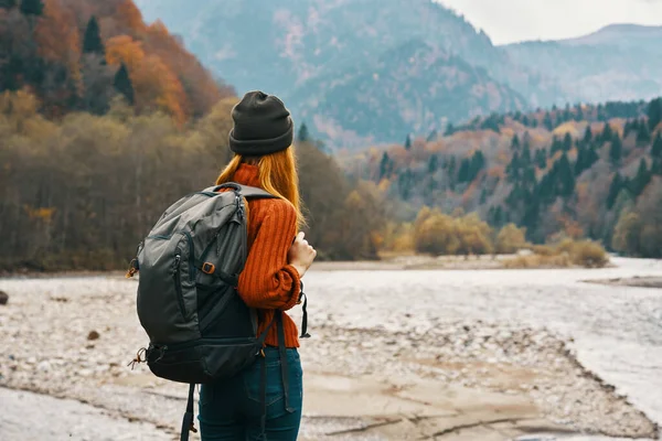 Mujer viaja en las montañas en otoño cerca del río en la naturaleza con una mochila vista trasera —  Fotos de Stock