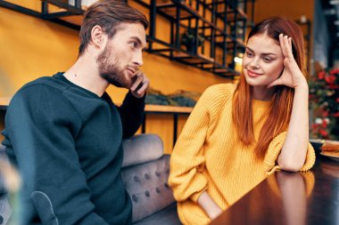 Bir kadın elleriyle hareket eder ve elinde saati olan yakışıklı bir adama bir şeyler söyler.