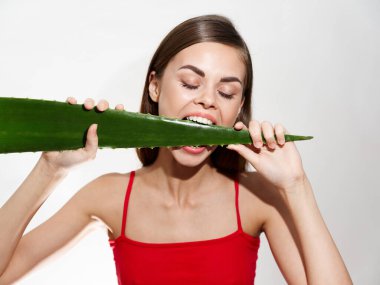 Güzel bir kadın beyaz dişli bir aloe yaprağını ısırır. Arka planda beyaz dişler ve kırmızı bir tişört mankeni vardır.