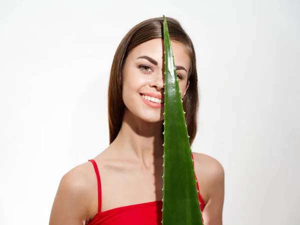 Szczęśliwa brunetka kobieta z zielonym liściem aloesu przed twarzą na jasnym tle — Zdjęcie stockowe