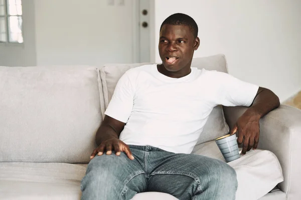 Chico de aspecto africano se sienta en el sofá y mira a un lado —  Fotos de Stock