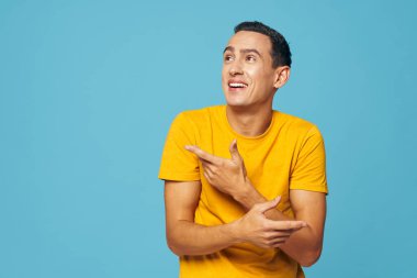 Sarı tişörtlü bir adam mavi arka planda kendine sarılıyor.