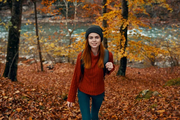 Un voyageur en pull rouge et un chapeau se promène dans la forêt d'automne près d'une rivière de montagne vue de dessus — Photo