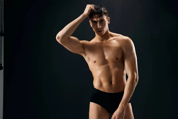 En man i mörka shorts med en muskulös kropp på en mörk bakgrund — Stockfoto