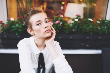 Kitaplı genç bir kadın kanepedeki sandalyede oturuyor. Baharatlı bir tişörtle. Siyah kravat modeli.