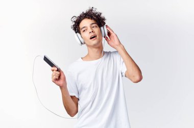 Beyaz tişörtlü, kıvırcık saçlı adam kulaklıklı telefon teknolojisiyle müzik dinliyor.