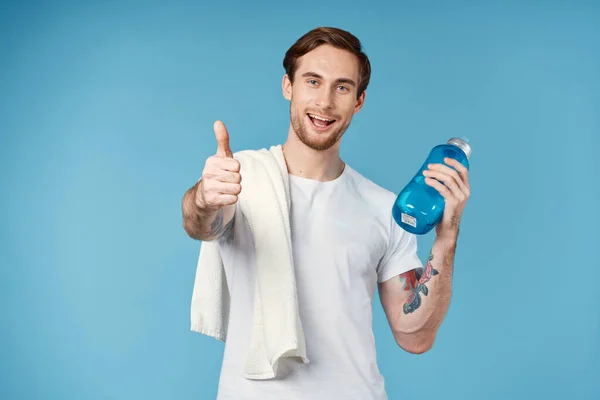 Uomo sportivo con tatuaggi sulle braccia bere bottiglia energia allenamento sfondo blu — Foto Stock