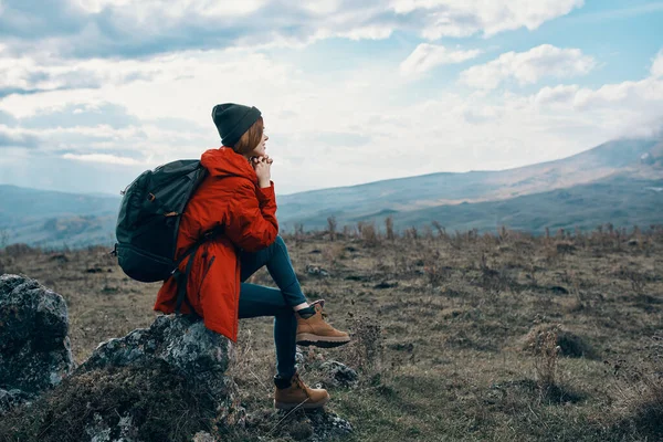 재킷을 입고 여행하는 여자가 큰 돌 위에 앉아서 경치를 바라본다 — 스톡 사진