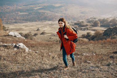 Ceket kotlu ve botlu bir gezgin doğada dağlara tırmanıyor.
