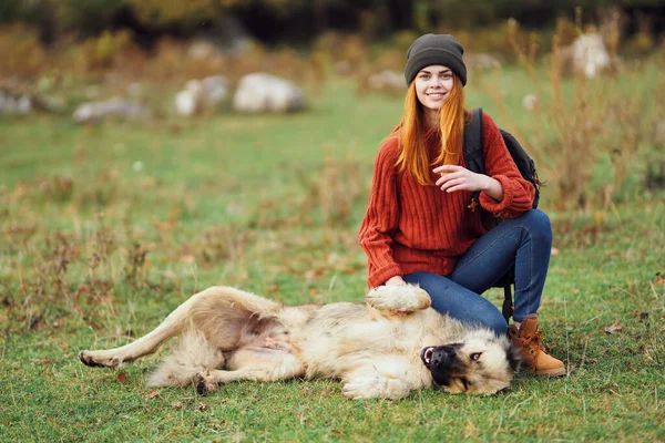 Woman hiker in the mountains lies on the grass next to the dog playing fun — Stock Photo, Image