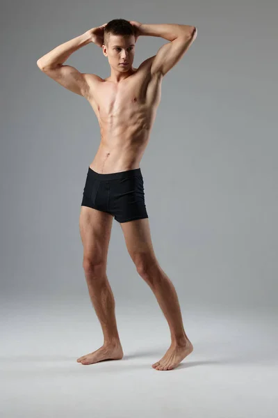 Atleta em shorts pretos mantém as mãos atrás de sua cabeça nu torso cinza quarto full-length modelo espaço de cópia — Fotografia de Stock