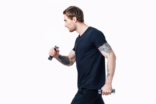 Hombre deportivo con mancuernas sobre fondo blanco su tatuaje en el brazo negro camiseta recortada vista — Foto de Stock