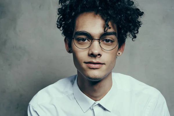 Portrait of a nice guy with curly hair on a gray background and a light shirt glasses model close-up — Stock Photo, Image