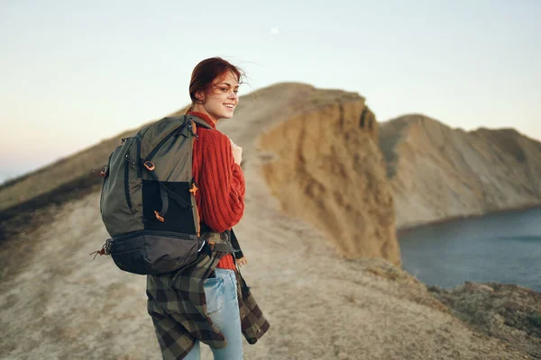 Felice viaggiatore donna a riposo in montagna vicino al mare e vista posteriore di uno zaino modello — Foto Stock