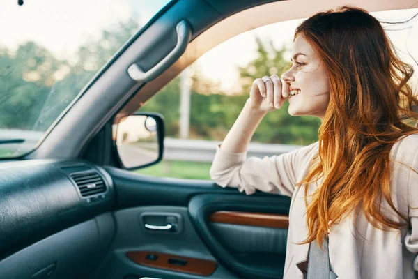 Mulher feliz com cabelo vermelho no banco da frente do carro tocando o rosto com as mãos cortadas vista — Fotografia de Stock