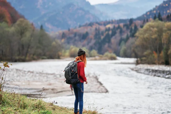 Femme randonneur avec les mains levées sur la rive de la rivière dans les montagnes en automne sur la nature — Photo