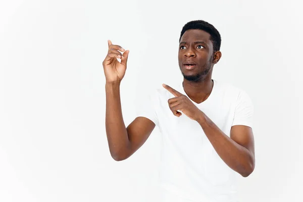 Carino africano uomo in bianco t-shirt gesturing con le mani su sfondo chiaro — Foto Stock