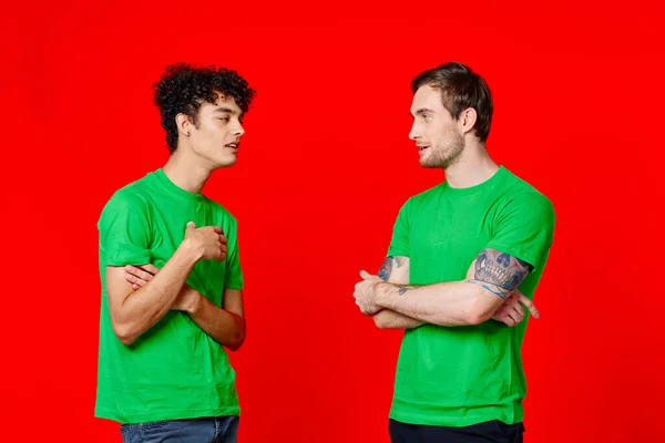 Dos amigos en camisetas verdes están de pie al lado de la comunicación positiva fondo rojo — Foto de Stock