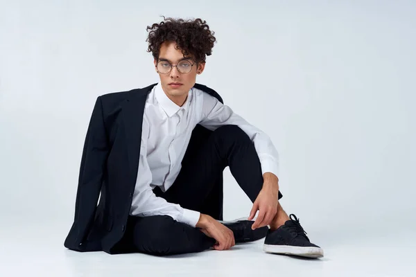 Un tipo con un traje clásico y gafas se sienta en el suelo en una habitación luminosa —  Fotos de Stock