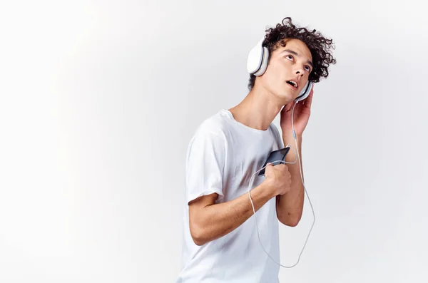 Άνθρωπος με σγουρά μαλλιά σε λευκό t-shirt ακούγοντας μουσική με ακουστικά τεχνολογίας τηλέφωνο — Φωτογραφία Αρχείου