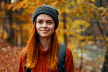 portrait of a beautiful woman in a hat sweater with a backpack on her back in the autumn forest in nature clipart