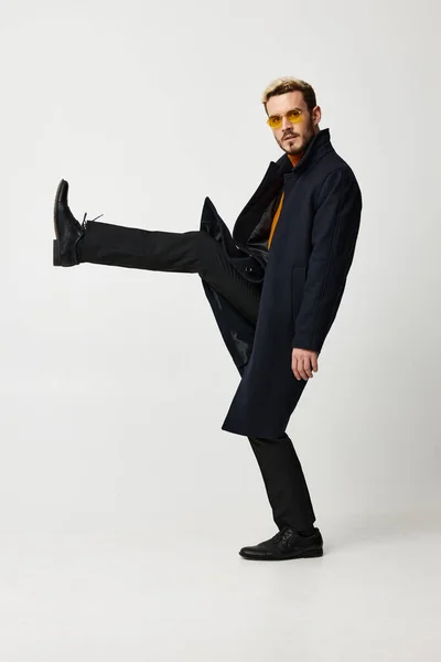 Fashionable man in a coat lifted his leg up and glasses on his face side view — Stock Photo, Image