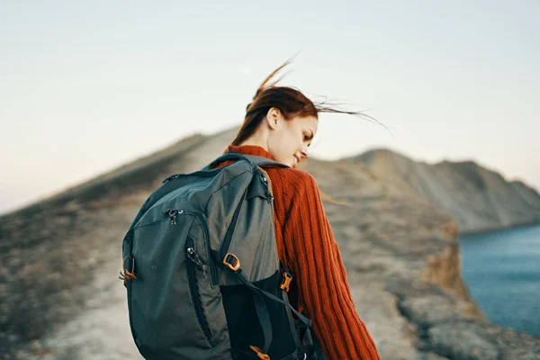 Donna sale le montagne vicino al mare con uno zaino sulla schiena guardando indietro — Foto Stock