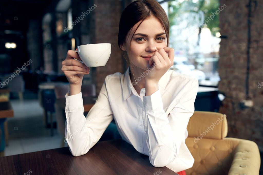 pretty business woman in white shirt sits in a cafe with a cup of coffee