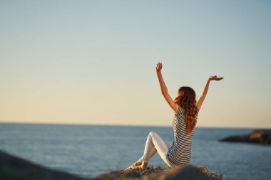 Nehrin kıyısında kollarını kaldırmış, geriye doğru bakan çizgili tişörtlü bir kadın.