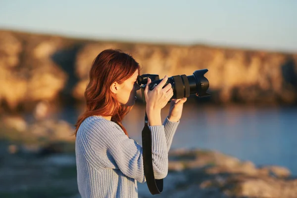 Donna con macchina fotografica al tramonto in montagna nella natura vicino al mare — Foto Stock