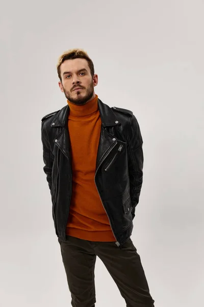 Coche de moda con una chaqueta de cuero y un suéter naranja sostiene sus manos detrás de un cinturón y pantalones marrones —  Fotos de Stock