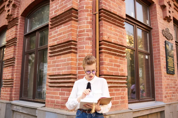 Φοιτήτρια με κοντά μαλλιά γυαλιά κοντά στο κτίριο τούβλο στο δρόμο και λευκό πουκάμισο γραβάτα περικοπή άποψη — Φωτογραφία Αρχείου