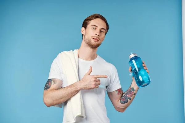 Спортивний чоловік з татуюваннями на руках п'є пляшку енергії тренування синій фон — стокове фото