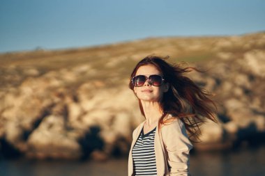 Yazın dağlarda güneş gözlüğü takan kızıl saçlı bir kadının portresi.