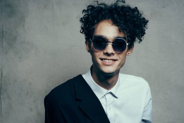 Gözlüklü ve omuzunda ceketi olan şık kıvırcık saçlı esmer adam.