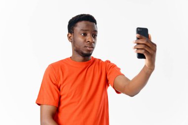 Afrikalı görünümlü yakışıklı bir adam arka planda yüzünün önünde bir cep telefonu tutuyor.