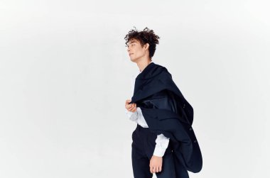 Kıvırcık saçlı ve klasik takım elbiseli bir adam elinde bir ceket tutuyor.