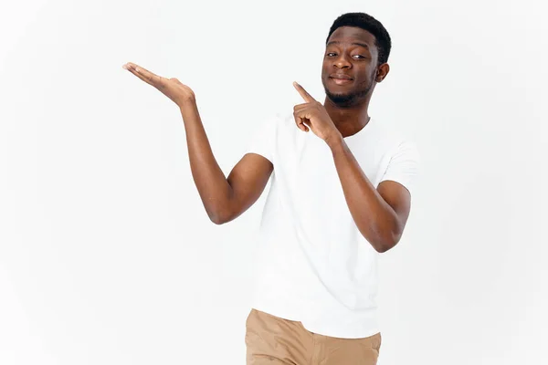 Beyaz tişörtlü tatlı Afrikalı adam, elleri arka planda açık bir şekilde el kol hareketi yapıyor. — Stok fotoğraf