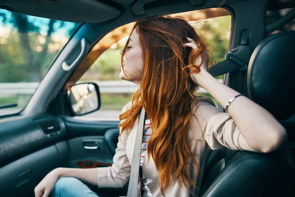 Mujer pelirroja feliz en un abrigo beige en el asiento delantero de un modelo de sonrisa de coche gesticulando con sus manos compañero de viaje — Foto de Stock