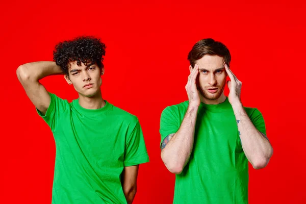 Due uomini che tengono la testa in magliette verdi su sfondo rosso — Foto Stock
