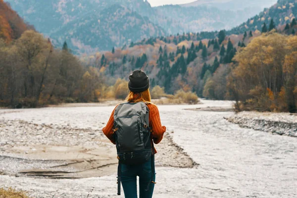 Senderista mujer feliz con una mochila en la orilla del río mirar a las montañas y la naturaleza del bosque de otoño —  Fotos de Stock