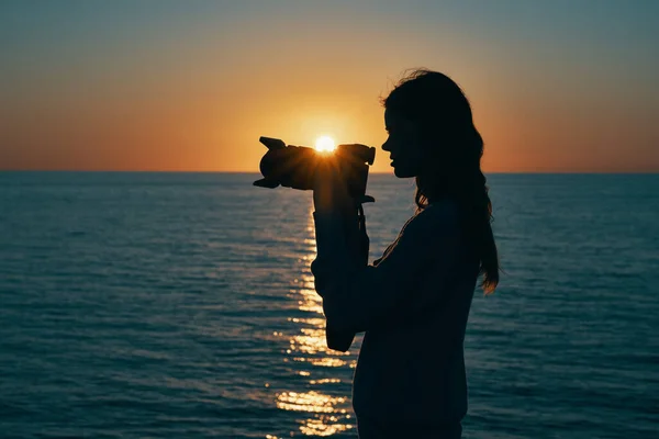 Woman photographer silhouette at sunset near the sea side view — Stock Photo, Image