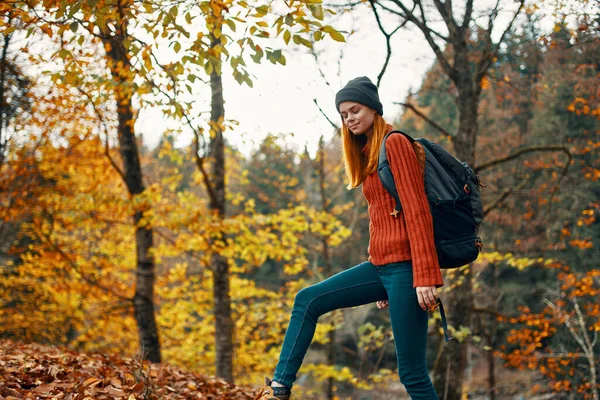 Mulher feliz caminhante com uma mochila em suas costas em jeans e uma camisola vermelha na paisagem parque floresta outono — Fotografia de Stock