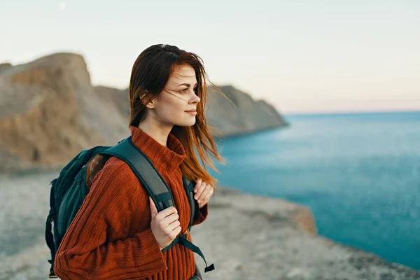 Bella donna in un maglione con uno zaino sulla schiena vicino al mare in montagna nella natura — Foto Stock