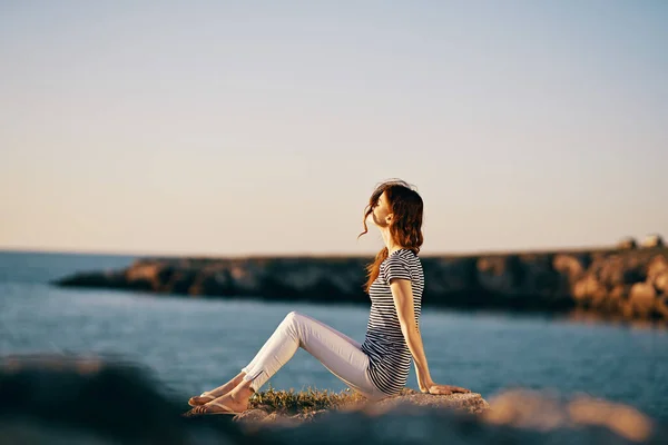 Donna in riva al mare siede su una grande vista laterale in pietra — Foto Stock