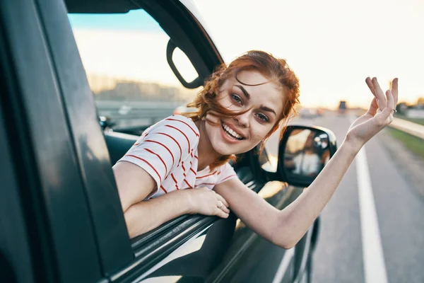 Mujer alegre con el pelo rojo mira por la ventana del coche en la carretera en vacaciones de verano relajarse — Foto de Stock