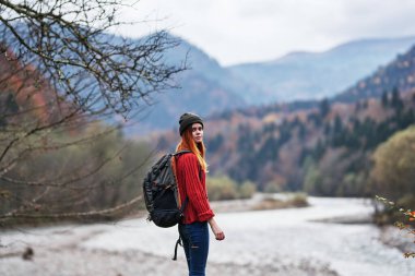 Sırt çantalı mutlu kadın nehir kıyısındaki dağlarda dinleniyor sonbahar manzarası temiz hava.