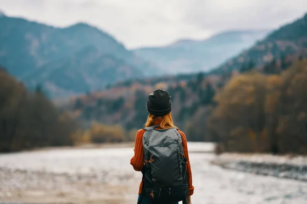 Femme sur la rive de la rivière avec sac à dos Voyage randonnée montagnes au loin — Photo