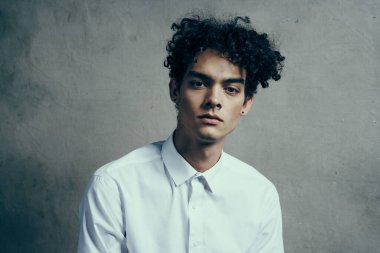 Yakışıklı, kıvırcık saçlı, beyaz gömlekli, modern görünüyor.